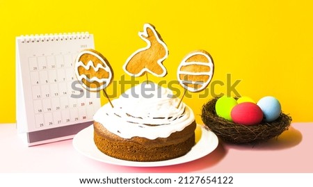 The concept of spring holiday bright Easter, traditions.  On a yellow background, close-up is an Easter cake decorated with cookies.  Multi-colored eggs in a bird's nest, April calendar.