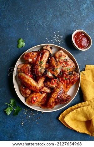 Grilled spicy chicken wings with ketchup on a plate on a dark blue slate, stone or concrete background. Top view with copy space. Royalty-Free Stock Photo #2127654968
