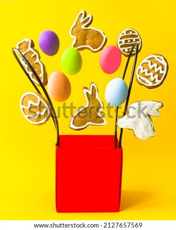 On a yellow background, there is a red box, a packaging bag from which colorful Easter eggs and delicious homemade cookies fly out.  The concept of holiday sales, sales, confectionery.
