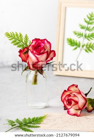 Romantic flower arrangement with red roses and green fern leaves in glass vase. Floral still life in vintage style. Floristic or home deco concept. Copy space.
