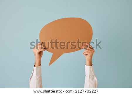Anonymous man holding over his head blank mockup of free speech bubbles with place for text on light blue background. Close up of paper card layout for notification of message, opinion or dialogue. Royalty-Free Stock Photo #2127702227