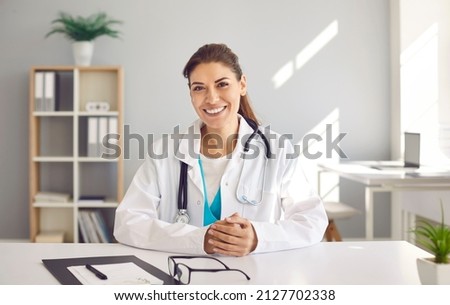 Portrait of happy beautiful Caucasian female doctor who has her own practice. Smiling European physician or cardiologist in white lab coat uniform sitting at desk in her modern office Royalty-Free Stock Photo #2127702338