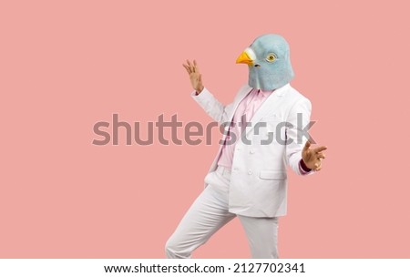Funny man wearing a pigeon mask dancing and having fun at a crazy fancy dress party. Weird guy ina bird mask dancing isolated on a solid pastel pink colour text copyspace background Royalty-Free Stock Photo #2127702341