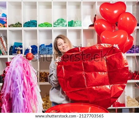 aerodesigner. a woman holds in her hands a large unblown red ball of foil in the shape of a heart. valentine's day. sale of balloons and compositions for festive decoration. 