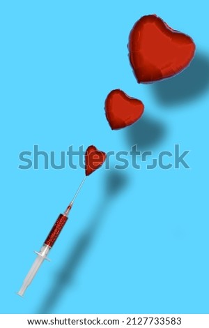 Balloons of red foil in the shape of a heart on a blue background come out of a syringe filled with red glitter. Minimal concept. It can symbolize love, health, vaccination ... 