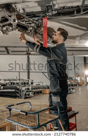 Bearded man maintenance technician tightening bolt with wrench while repairing aircraft in hangar Royalty-Free Stock Photo #2127740786