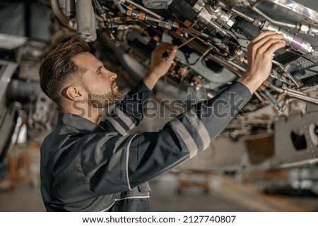 Bearded young man aviation mechanic checking aircraft components while working in repair station Royalty-Free Stock Photo #2127740807