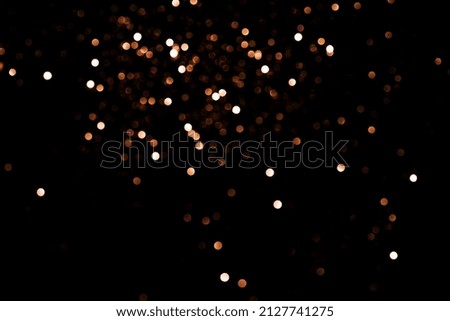 Falling gold colored confetti against black background.