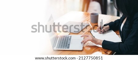 young businesswoman in suit using laptop computer and writing business papers at desk in modern coworking office. copy space.