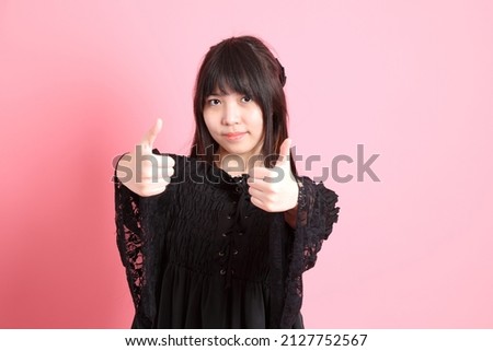 The cute young Asian girl with gothic dressed standing on the pink background