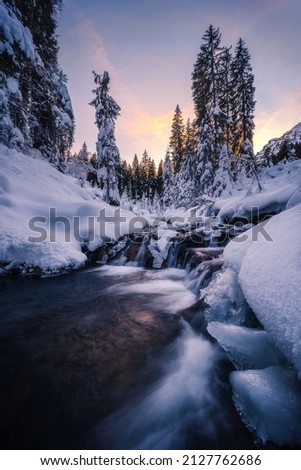 Winter sunset on a river crossing a snowy landscape, in Morgins, Valais, Switzerland Royalty-Free Stock Photo #2127762686