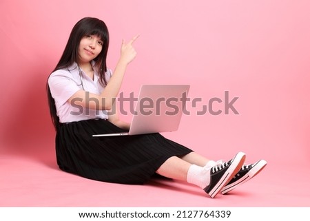 The teen Asian girl with university uniform sitting on the pink background.
