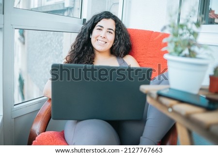 Relaxed plus size curly young woman smiling to camera while using a laptop to prepare,post and do training online. Training clothes. Getting fit for the summer concept. Beach body preparation