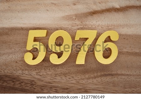 Wooden  numerals 5976 painted in gold on a dark brown and white patterned plank background.