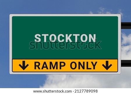 Stockton logo. Stockton lettering on a road sign. Signpost at entrance to Stockton, USA. Green pointer in American style. Road sign in the United States of America. Sky in background