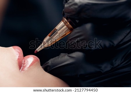Process applying permanent makeup tattoo of red on lips woman in beautician salon.