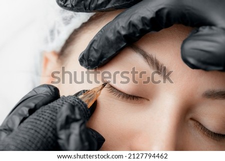 Permanent tattoo makeup on eyelashes of eyes of young woman in beauty salon. Royalty-Free Stock Photo #2127794462