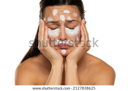 Unhappy sad woman posing with face cream on a white background Royalty-Free Stock Photo #2127838625