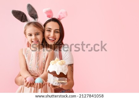 Little girl, her mother with tasty Easter cake and eggs on pink background Royalty-Free Stock Photo #2127841058