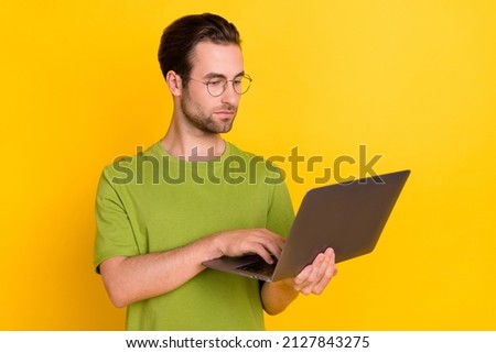 Photo of strict beard millennial guy type laptop wear eyewear green t-shirt isolated on yellow color background