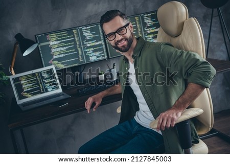 Photo of good mood cheerful young guy dressed khaki shirt glasses administrating computer systems indoors workshop workplace