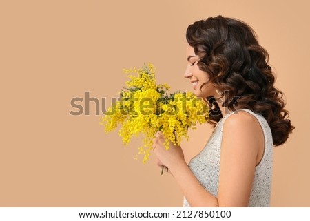 Beautiful young woman with mimosa flowers on color background Royalty-Free Stock Photo #2127850100