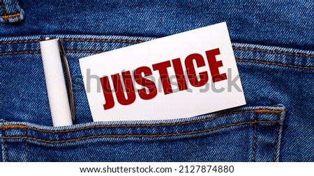 The back pocket of blue jeans contains a white pen and a white card with the text JUSTICE