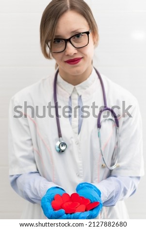Young pretty woman doctor in a white medical coat and rubber gloves with a phonendoscope holds a red heart in her hands in a hospital. Selective focus. Portrait
