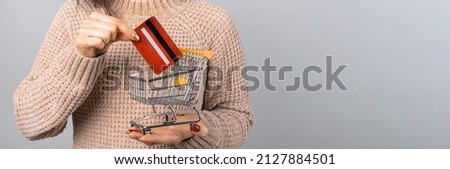 Close up photo of woman holding red credit card and shopping cart.