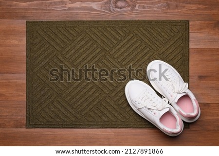 New clean door mat with shoes on wooden floor, flat lay Royalty-Free Stock Photo #2127891866