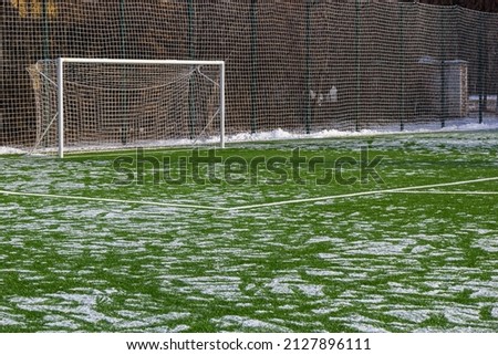 field for playing football in winter, artificial grass on cleared of snow in the distance gate and net.