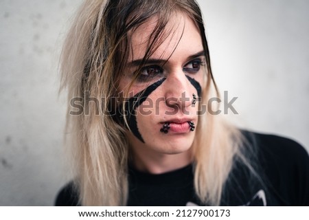 Headshot of an attractive emo punk young man with serious expression, looking away. Close up  of a pierced and face painted, long hair guy in his late 20s, isolated on white background. 