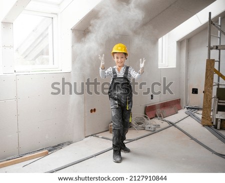 cool young boy with yellow safety helmet posing and having fun on construction building site indoor in a loft