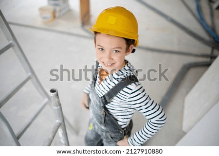 cool young boy with yellow safety helmet posing and having fun on construction building site indoor in a loft