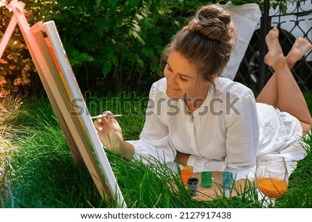 Artist painting on the easel outdoors in the garden. Open air outdoor art workshop. Draw on the canvas with brush and palette sitting on the grass during a picnic in a park