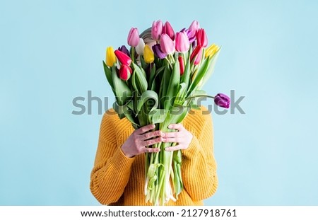 International Women's Day. pretty charming brunette young woman dressed yellow clothes holding tulip bunch isolated blue color background Royalty-Free Stock Photo #2127918761