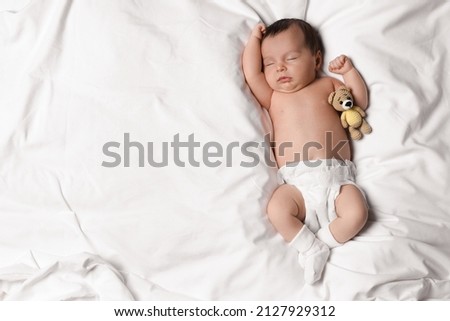 Cute little baby with toy bear sleeping on soft bed, top view. Space for text Royalty-Free Stock Photo #2127929312
