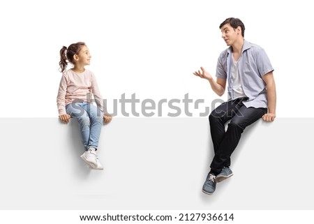 Young man sitting on a blank panel and talking to a child isolated on white background Royalty-Free Stock Photo #2127936614