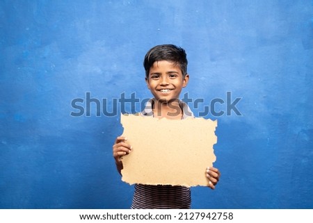 Smiling kid showing empty sign board or placard by looking at camera on blue background - cocnept of promotion, advertisement and Poverty Royalty-Free Stock Photo #2127942758