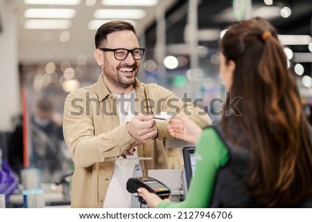 A smiling man giving credit card to a cashier and paying for groceries in supermarket. Royalty-Free Stock Photo #2127946706