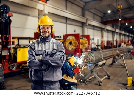 Portrait of metallurgy worker standing in factory and smiling at the camera. Royalty-Free Stock Photo #2127946712