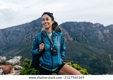 Portrait of a smiling woman relaxing during a mountain hike. Female with analog camera and backpack enjoying the view while standing on the top of the mountain. Royalty-Free Stock Photo #2127960269