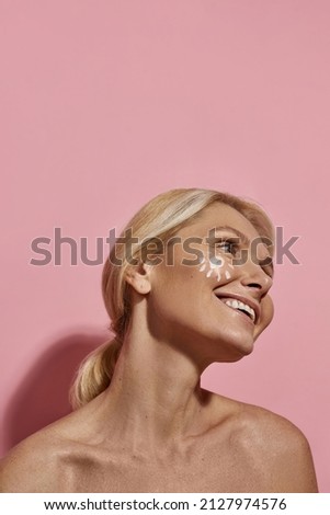 Partial image of mature caucasian woman with sun picture from sun cream on her face. Joyful blonde female person looking away. Body and skin care. Isolated on pink background. Studio shoot. Copy space