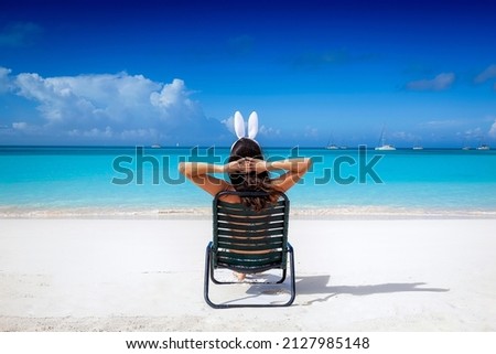 A woman with easter bunny ears relaxes on a sunchair at a tropical paradise beach Royalty-Free Stock Photo #2127985148