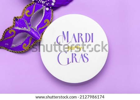 Mardi gras lettering. Congratulation card with mask on white podium on Violet background Top view 2022 Mardi Gras Parade Schedule