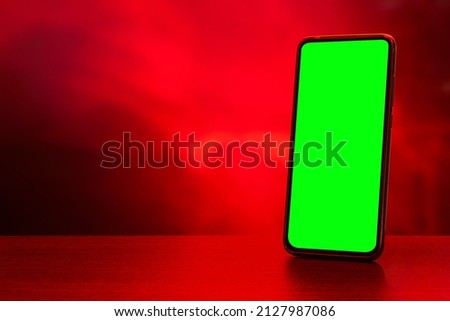 A closeup shot of a green screen on a mobile phone against a red blurry background