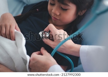 Asian woman pediatrician doctor hold stethoscope for exam a little girl patient and heck heart lungs of kid, Good family doctor visiting child at home, Healthcare and medicine for childhood concept. Royalty-Free Stock Photo #2127992300