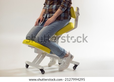 Woman is sitting on kneeling chair in office isolated on white. Ergonomic chair with wheels. Therapeutic stool with back support. Orthopaedic stool for desk based distance work from home. Royalty-Free Stock Photo #2127994295