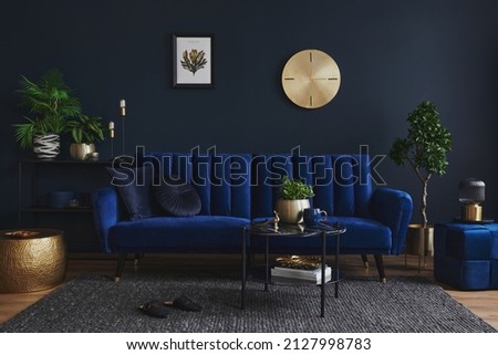 Stylish modern living room interior design with glamour blue sofa, metal shelf, coffee table, pouf and elegant home accessories. Dark blue wall. Home staging. Template. Copy space. Royalty-Free Stock Photo #2127998783