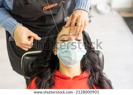 Close-up of a part of the face plucking eyebrows with a thread. Client with mask . High quality photo